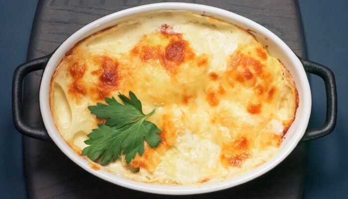 bubbly baked casserole with a golden brown crust and an herb garnish on a black countertop.