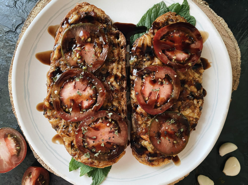 vegan cheesy tomato garlic bread on a white plate against a dark background