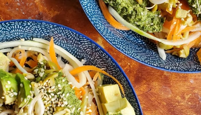 Raw noodles with pesto in two dishes against a wooden background