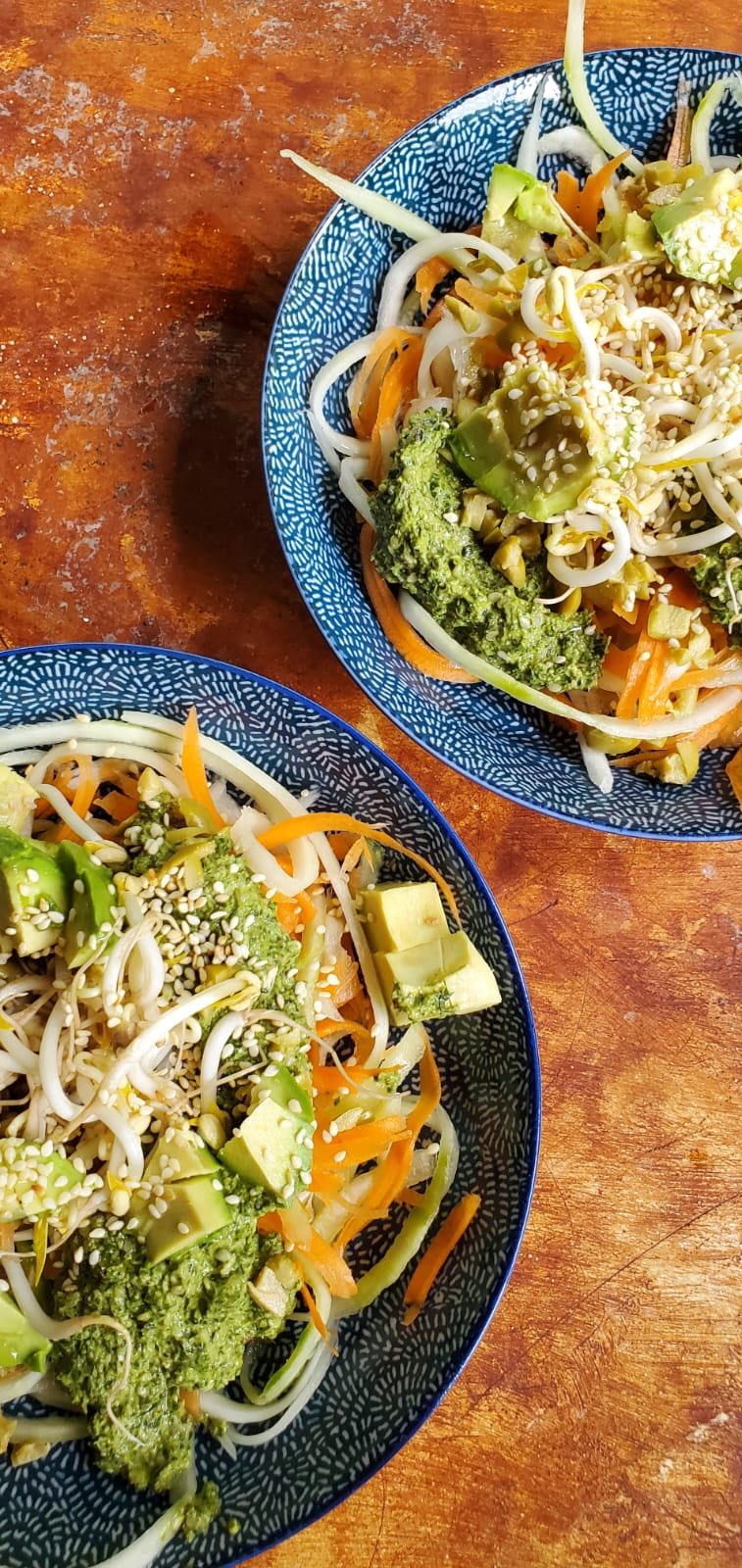 Raw noodles with pesto in two dishes against a wooden background