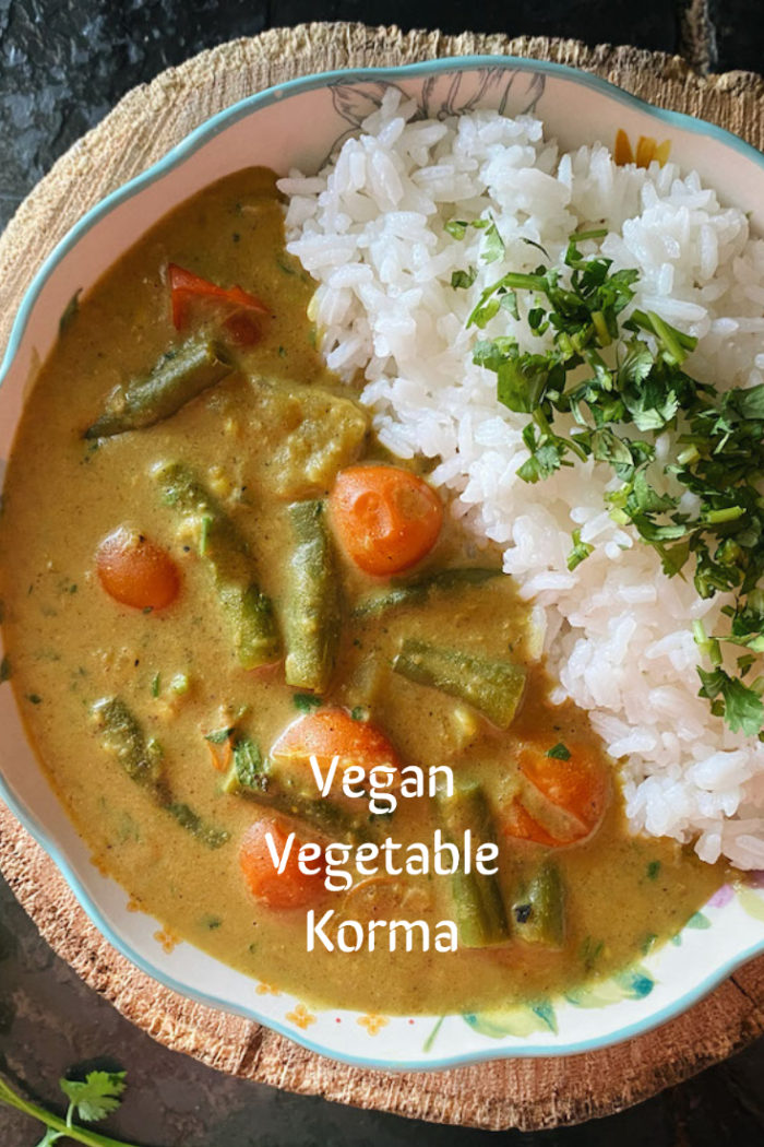 vegetable korma in a dish against a brown and black background with white caption