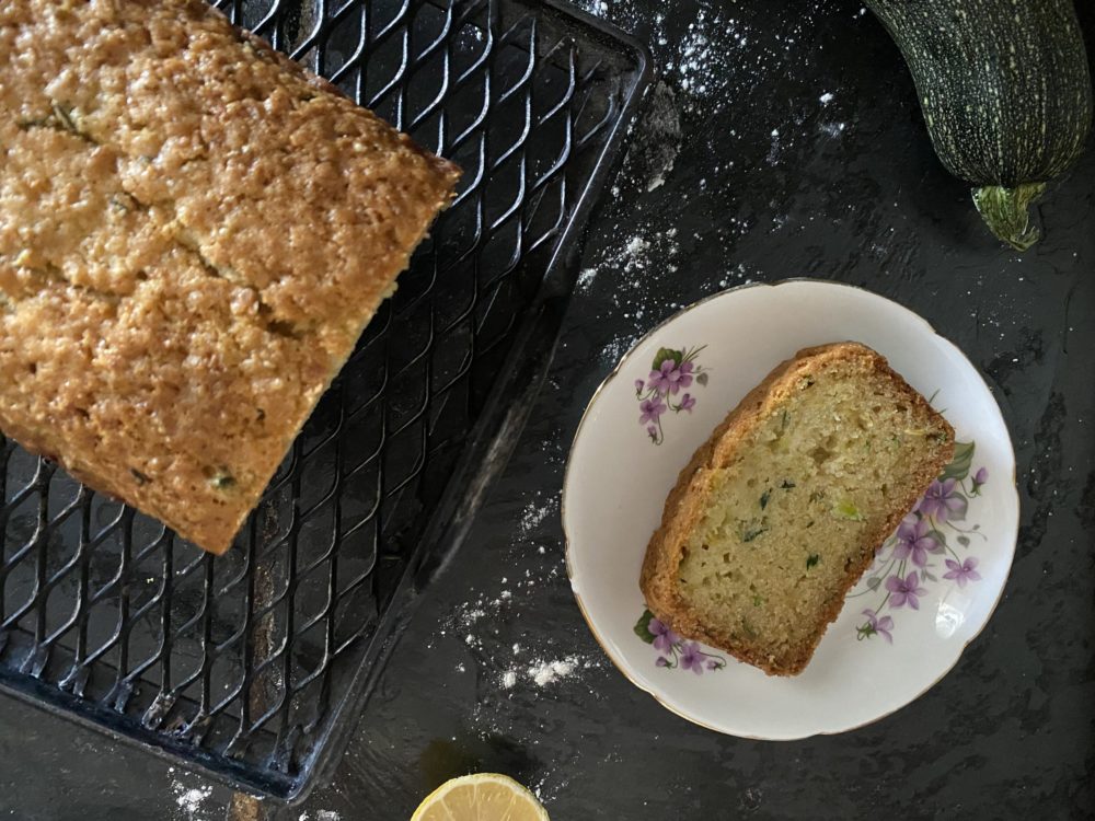 lemon zucchini bread on a white plate with purple flowers on a dark background