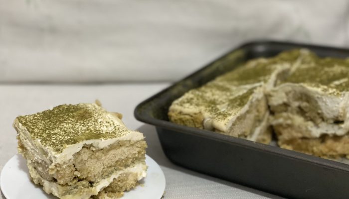 a slice of vegan matcha tiramisu on a white plate next to a black pan