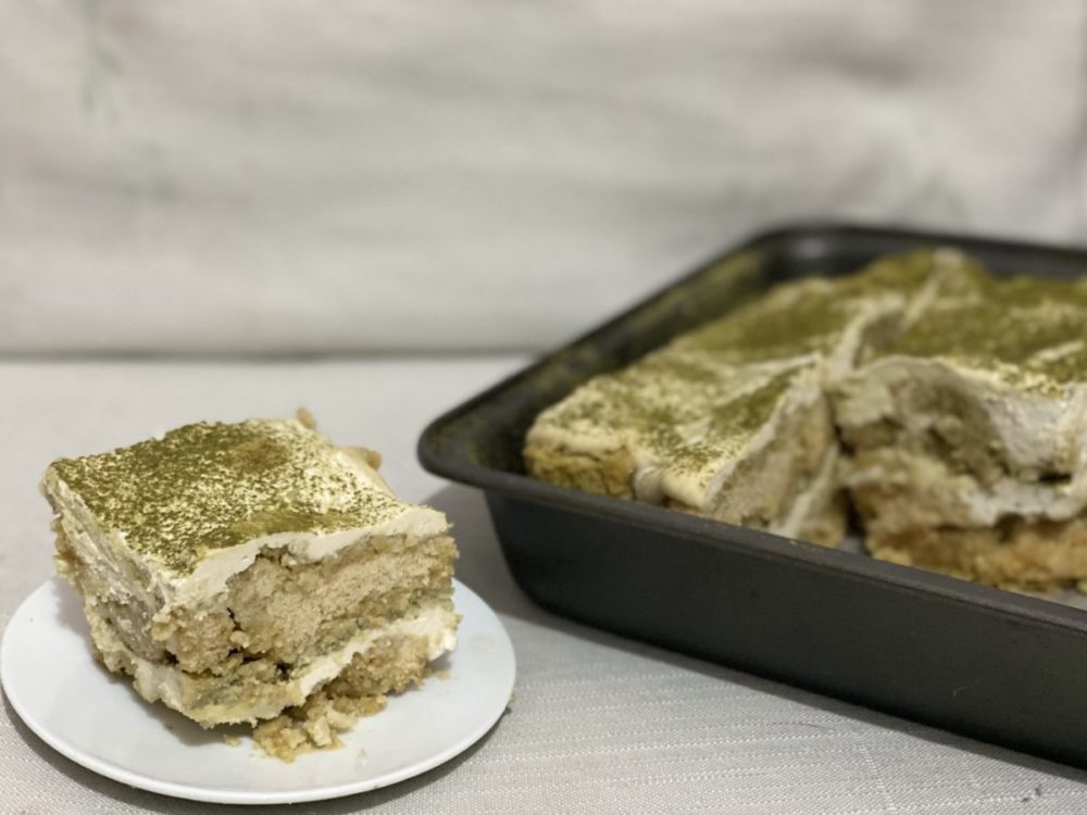 a slice of vegan matcha tiramisu on a white plate next to a black pan