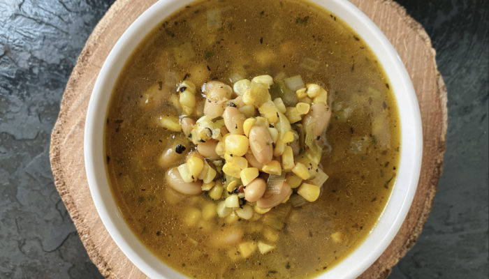 corn leek white bean soup in a white bowl with a brown and black background