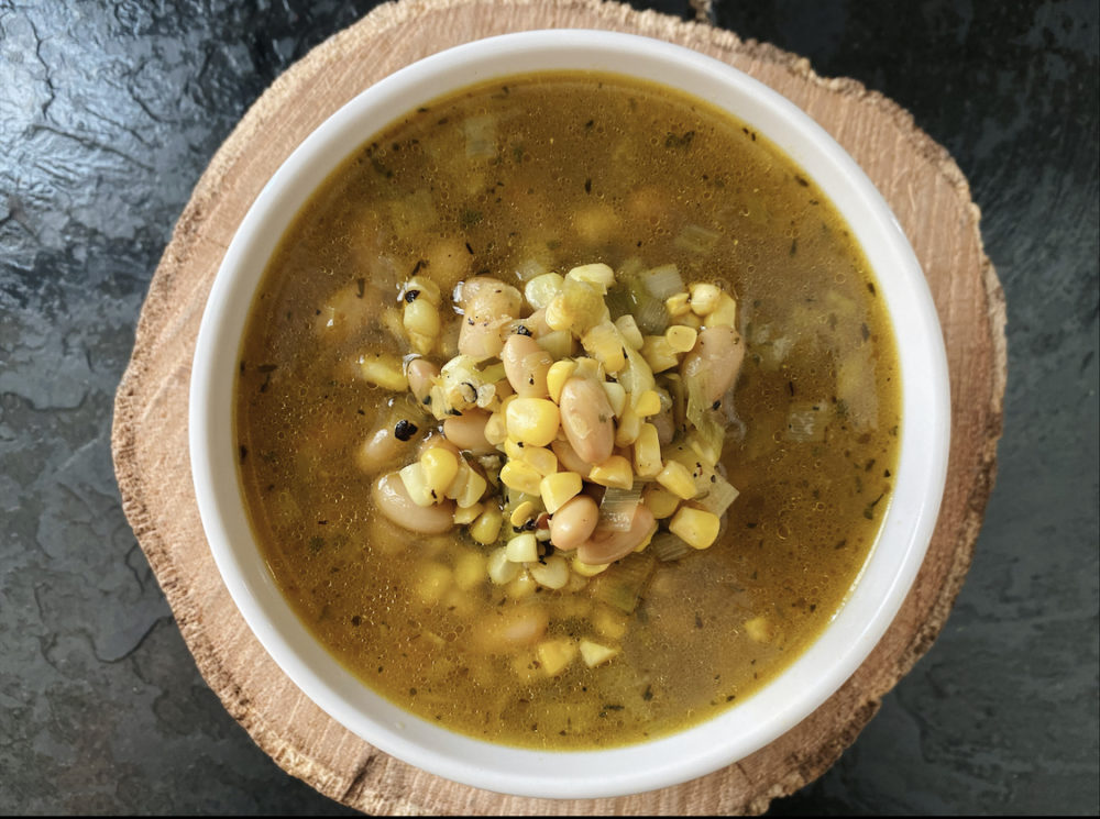 corn leek white bean soup in a white bowl with a brown and black background