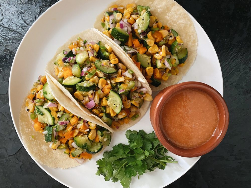 zucchini corn tacos on a white plate against a dark background