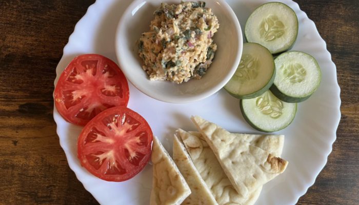 easy vegan crab cake dip, tomatoes, cucumbers, and pita bread on a white plate against a wooden surface