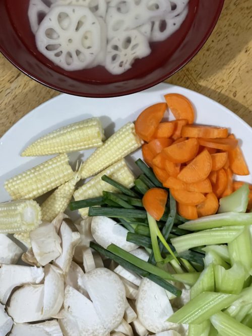 lotus root stir fry ingredients chopped on a white plate with lotus root in a red bowl