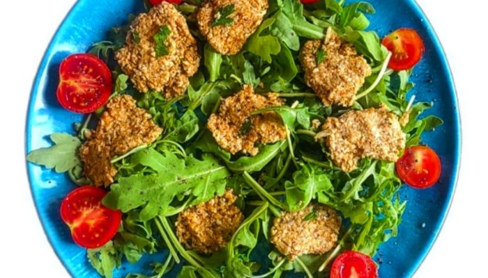 cauliflower bites surrounded by rucola and halved cherry tomatoes on a blue plate against a white background