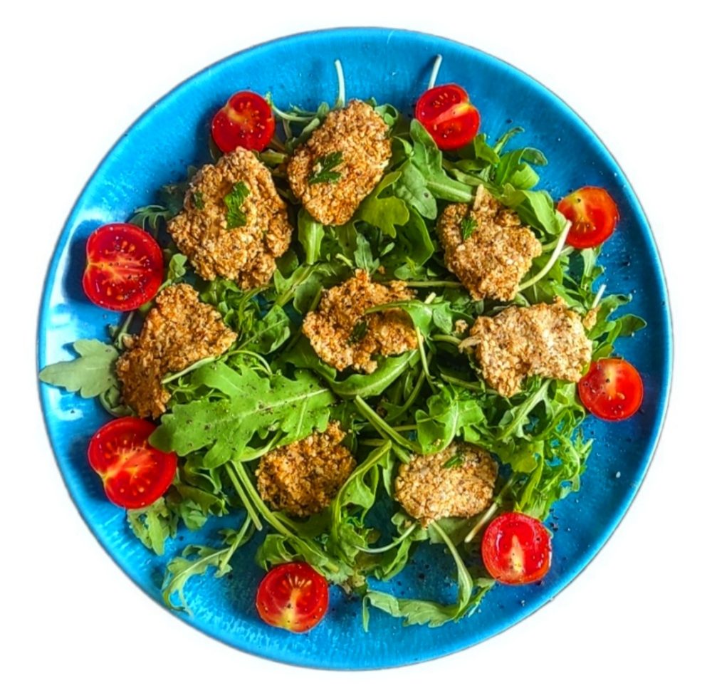 cauliflower bites surrounded by rucola and halved cherry tomatoes on a blue plate against a white background