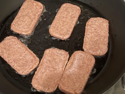 vegan spam frying in a dark pan