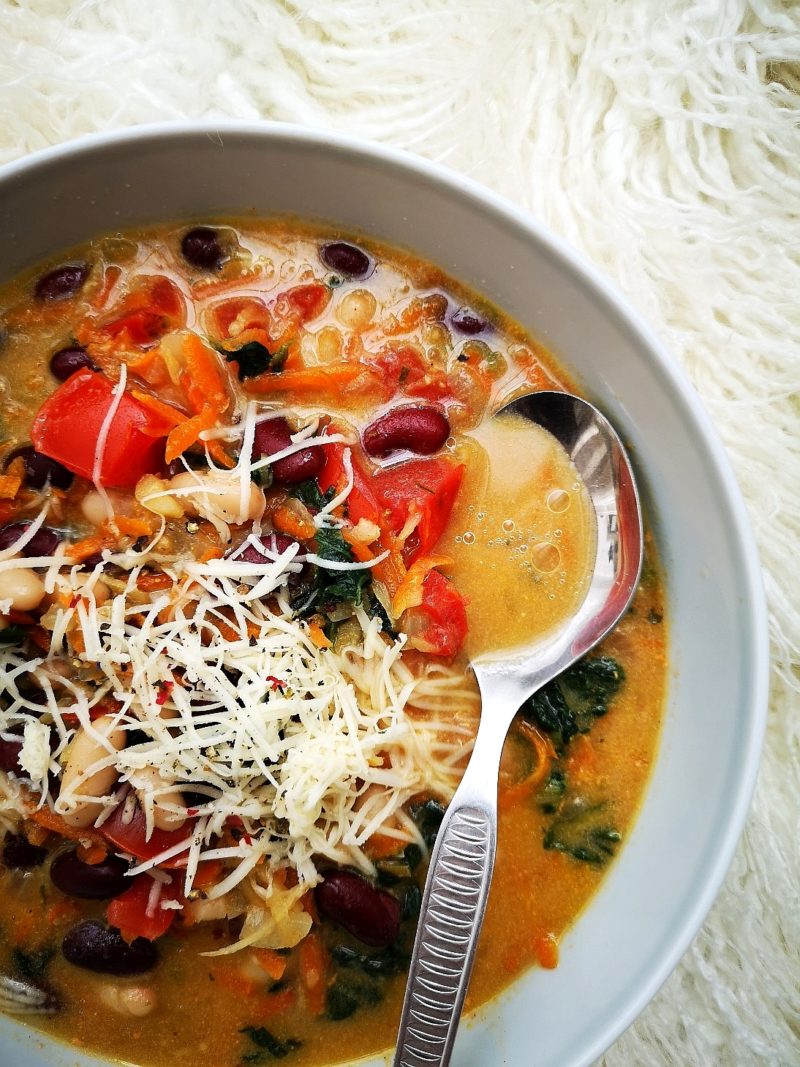 tuscan bread soup in a white bowl with a silver spoon; a white background