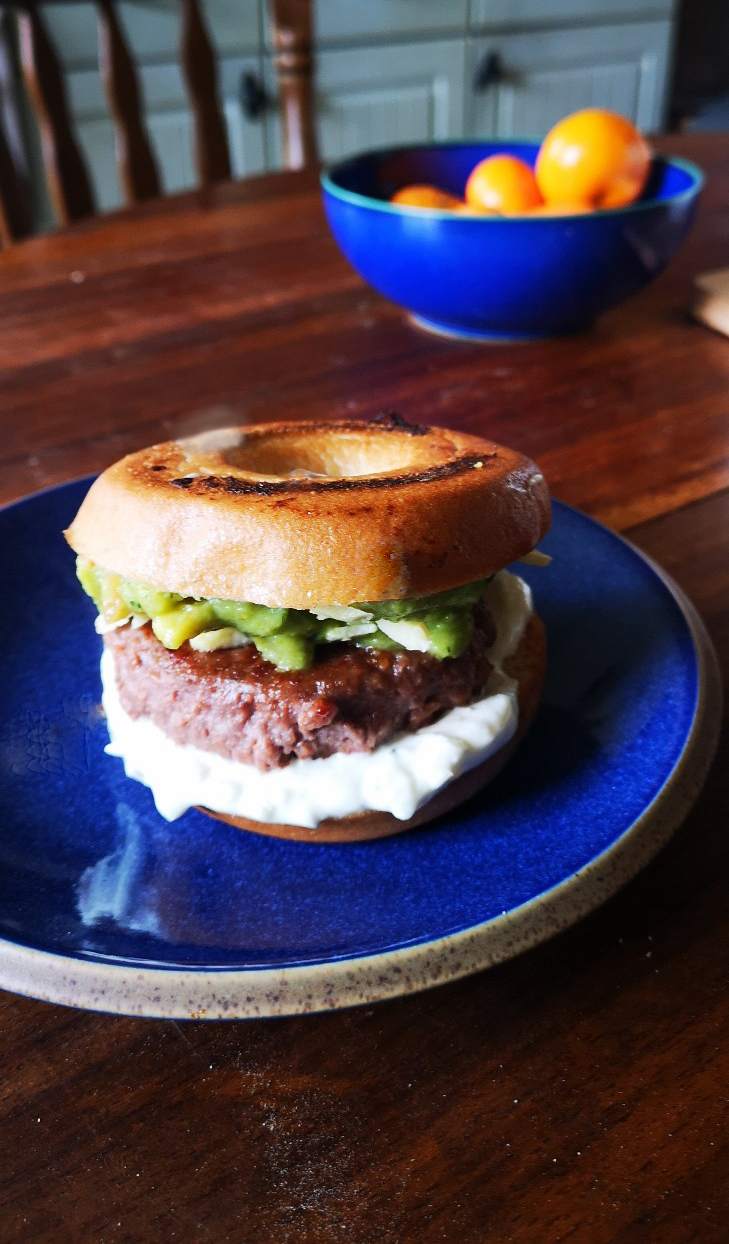 vegan breakfast bagel burger on a blue plate on a wooden table top