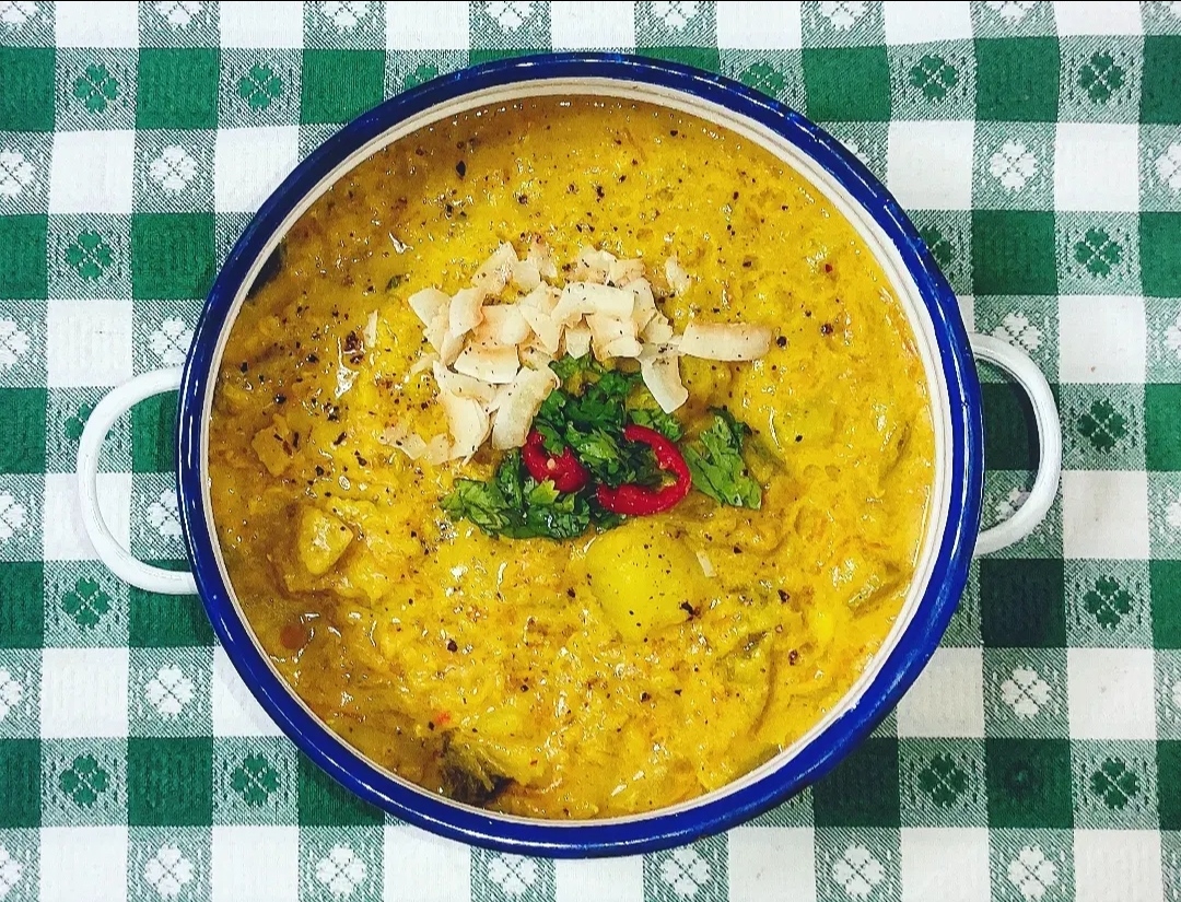spicy vegetable curry in a white and blue bowl against a green/white table top