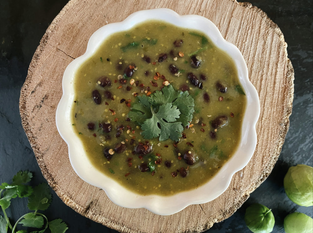 vegan tomatillo black bean soup in a white bowl with brown and black backgrounds