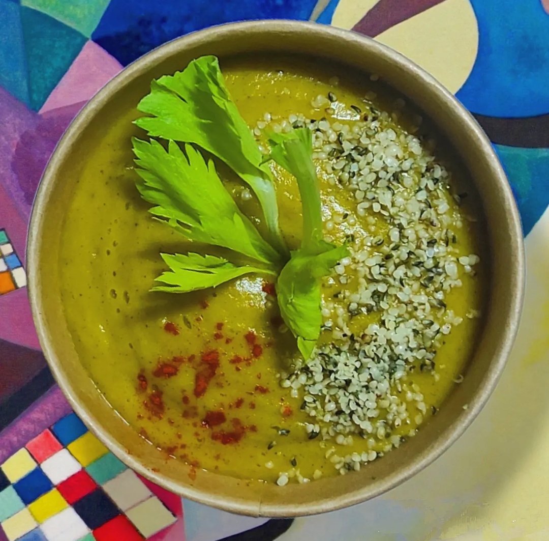 a bowl of green Nourish Me soup in a bowl against a colorful background