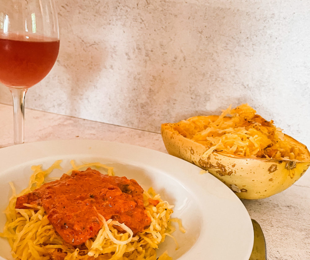 roasted red pepper squash noodles in a white dish in front of a drink and spaghetti squash