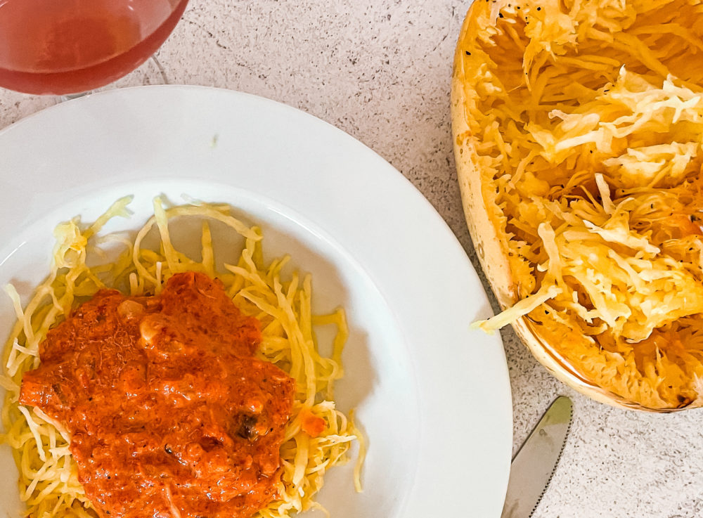 roasted red pepper squash noodles in a white dish next to a halved spaghetti squash