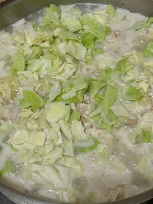 cabbage added to vegan chicken macaroni soup in a silver bowl