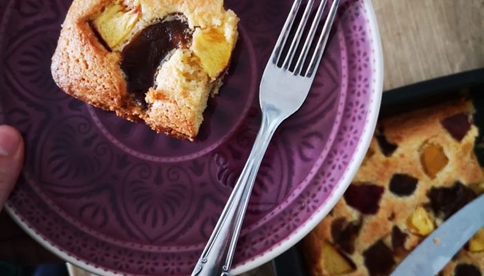 vegan nectarine plum cake in a purple dish with a silver fork on a wooden table