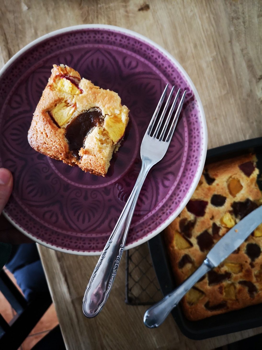 vegan nectarine plum cake in a purple dish with a silver fork on a wooden table