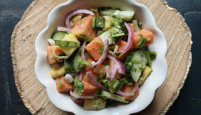 pineapple papaya salad in a white dish against a brown and black background