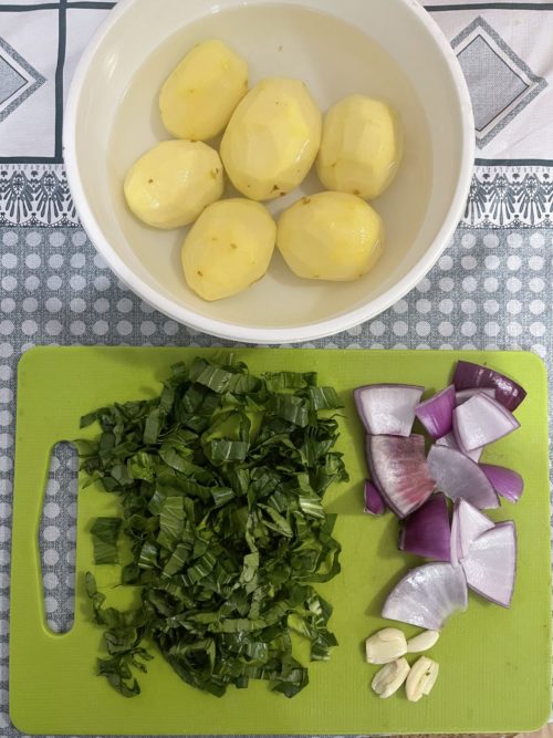 peeled potatoes in a white bowl; chopped vegetables on a green cutting board