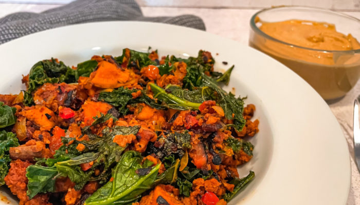 vegan sweet potato hash in a white dish in front of a clear bowl of orange sauce