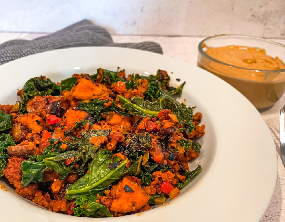 vegan sweet potato hash in a white dish in front of a clear bowl of orange sauce