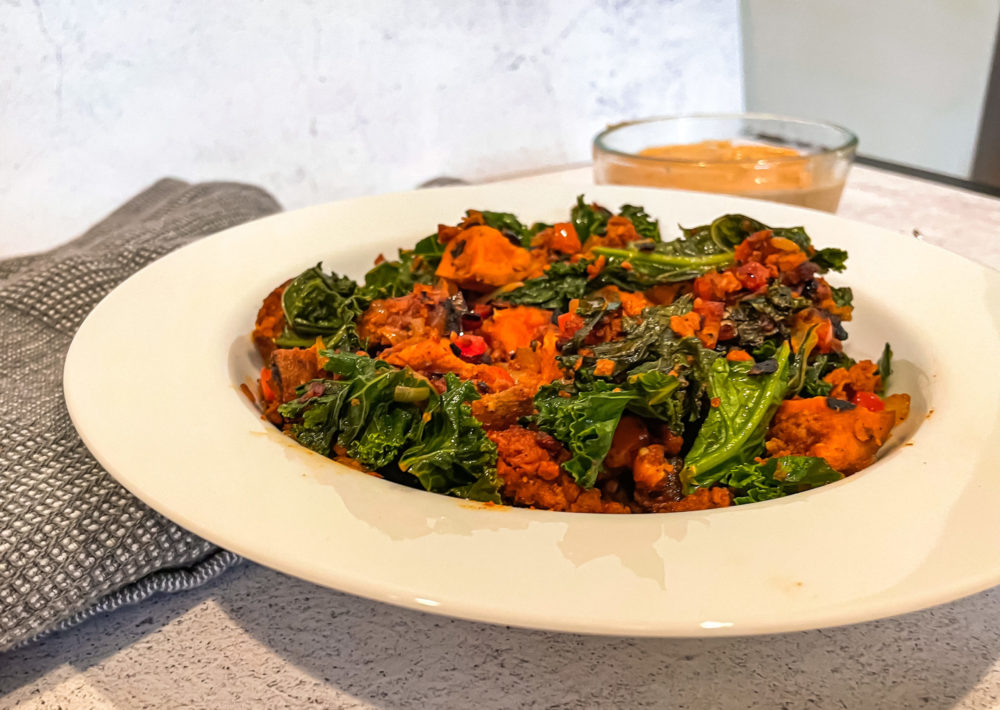 vegan sweet potato hash in a white dish in front of a clear bowl of orange sauce