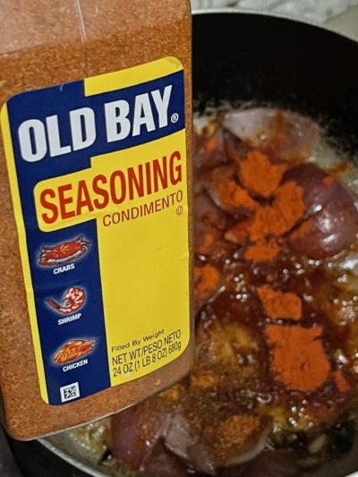 a container of old bay seasoning in front of cooking vegetables