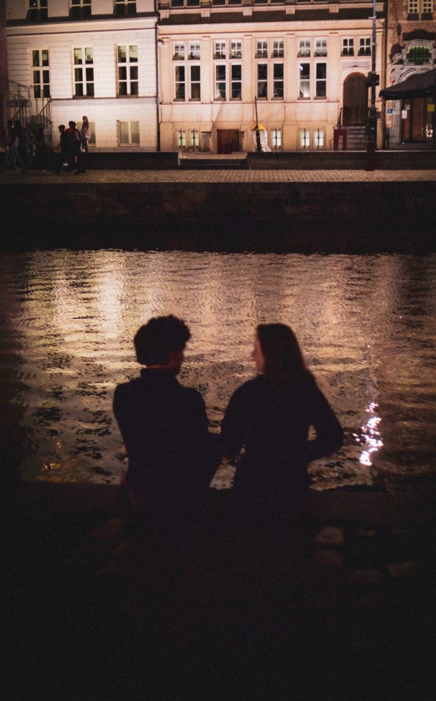 man and woman sitting on a quai looking at the water and silhouetted by the dim light.