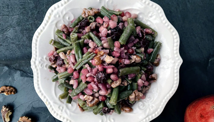 pomegranate cranberry green beans on a white plate against a dark background