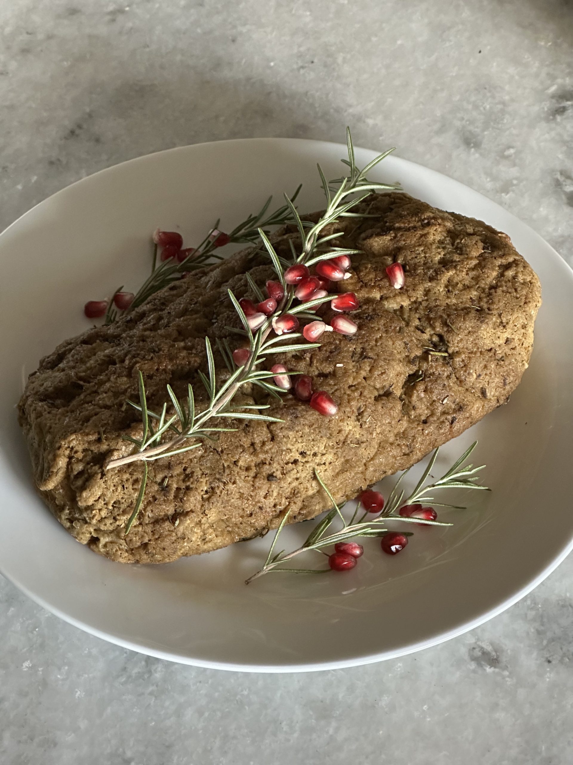 Vegan turkey on a white plate with pomegranate seeds and greens