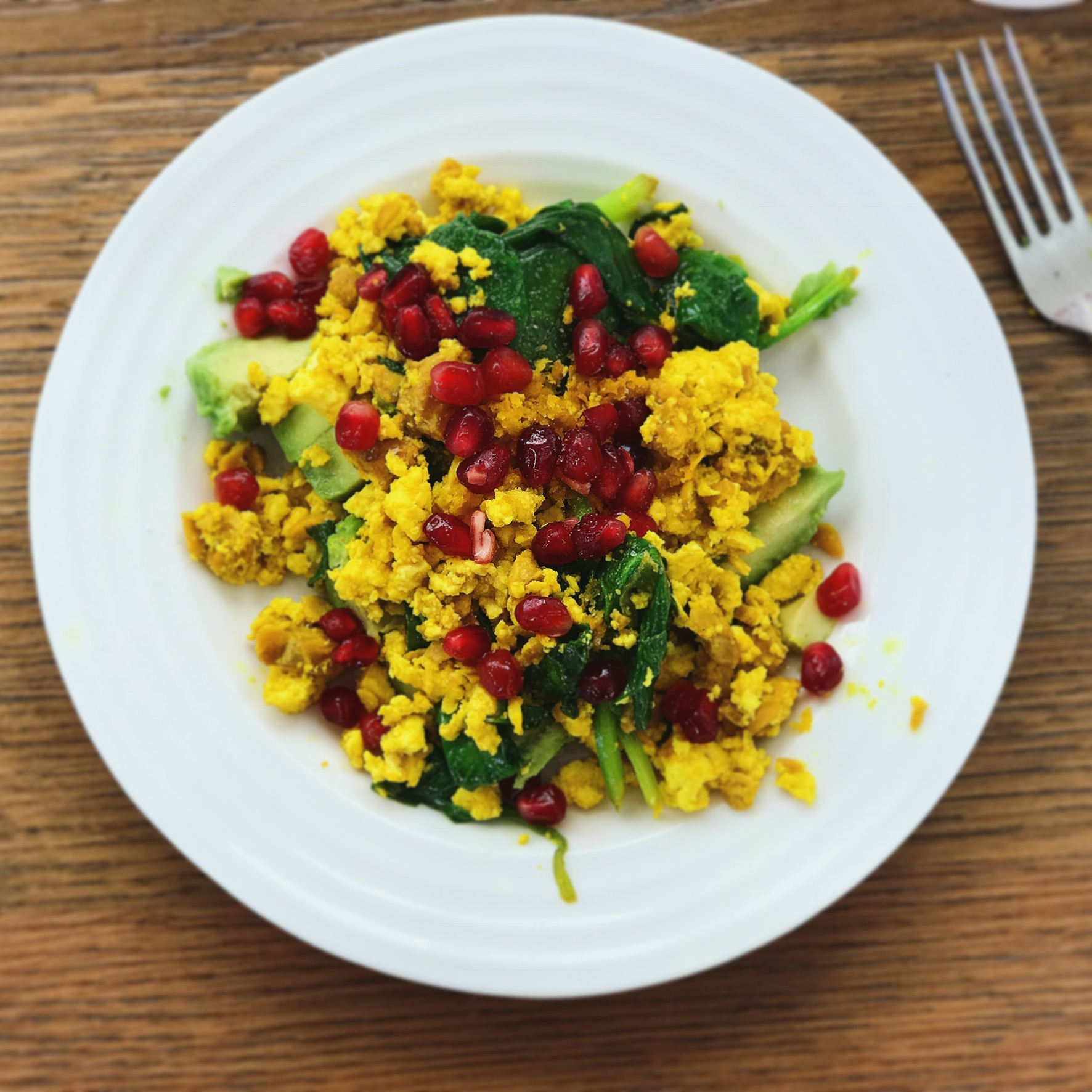 tofu scramble with pomegranate seeds on a white plate on a wooden table