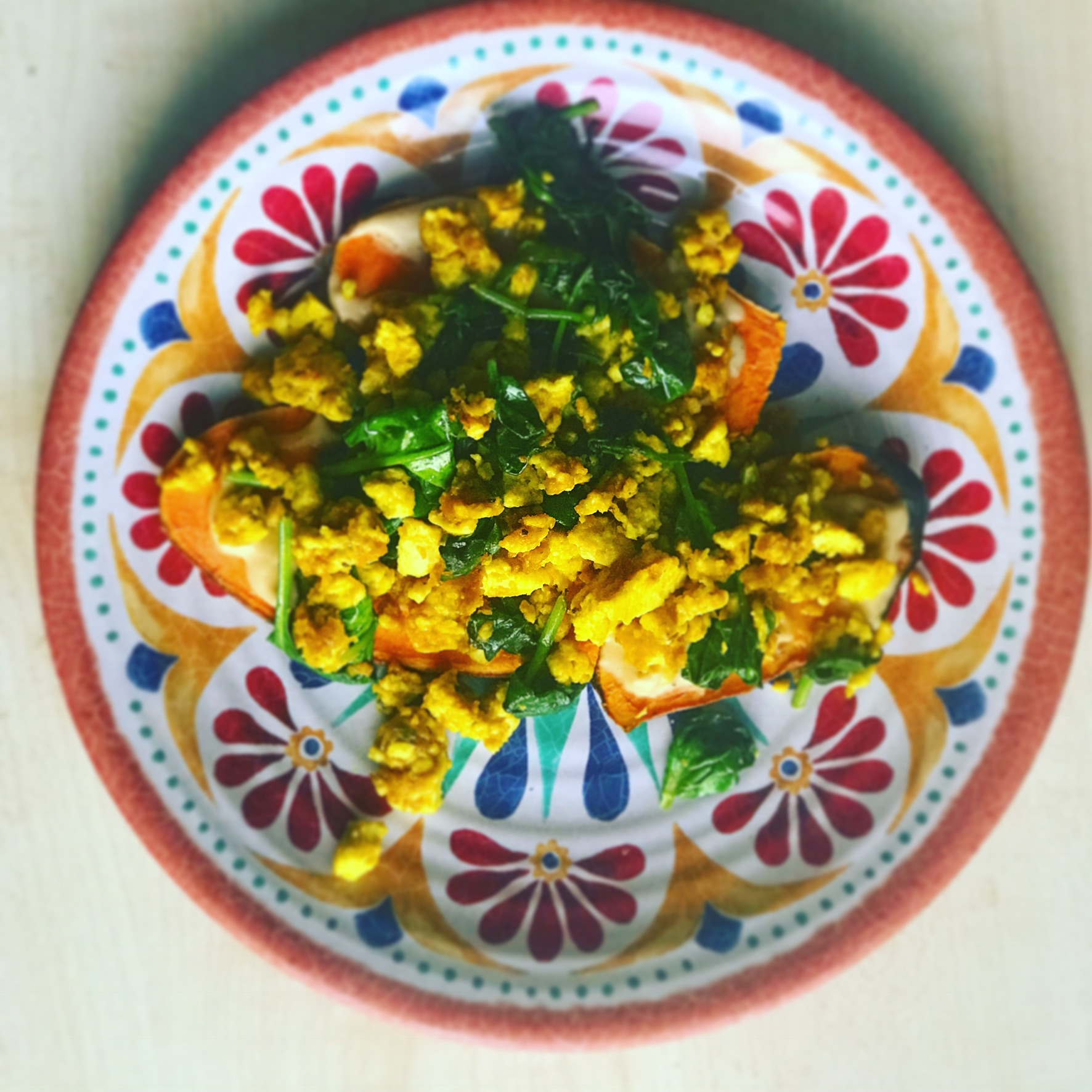 spinach tofu scramble on a colorful flower patterned plate on a white countertop.