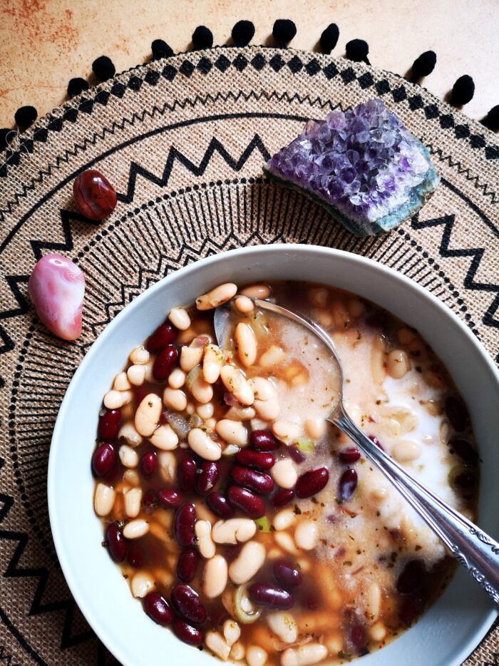 A bowl of bean soup in a white bowl on a decorative black and beige placemat and crystals