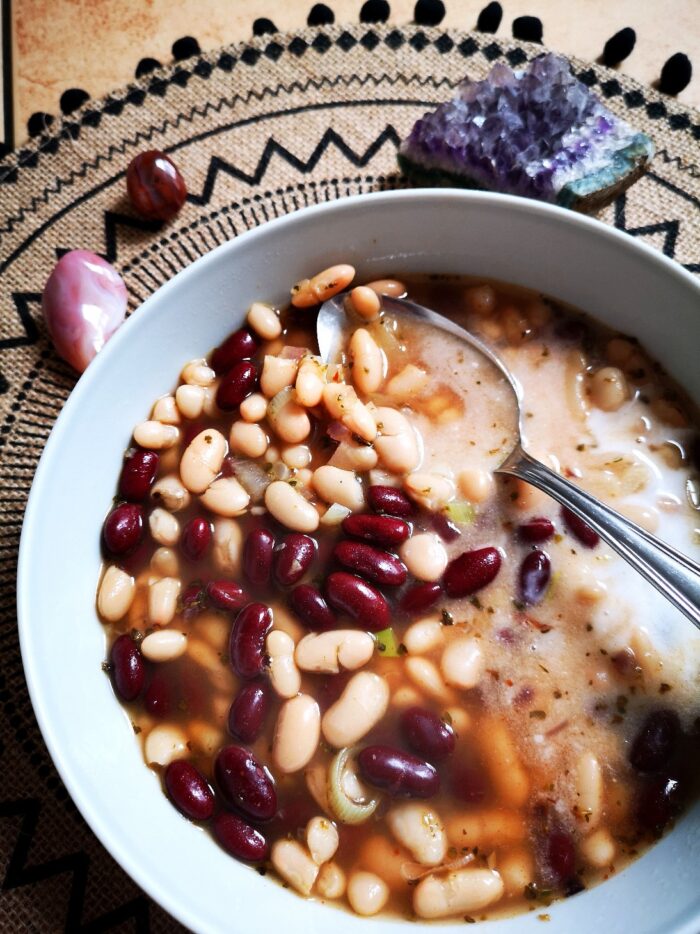 A bowl of bean soup in a white bowl on a decorative black and beige placemat and crystals