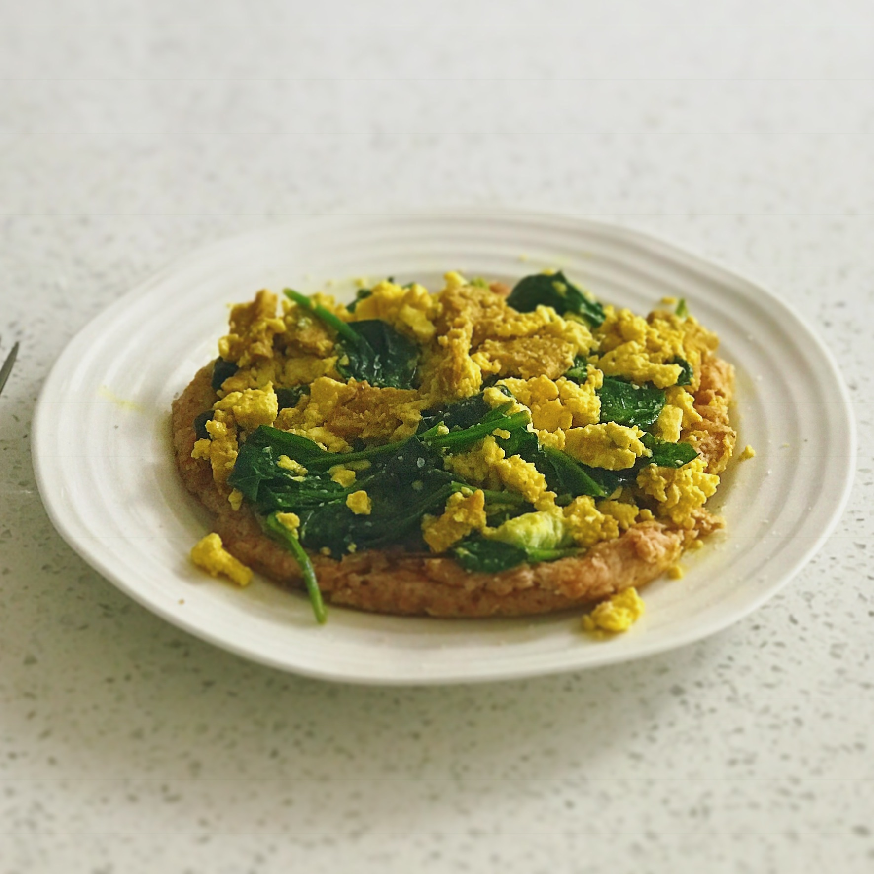 turmeric flavored tofu scramble with spinach on a white plate on white countertop.