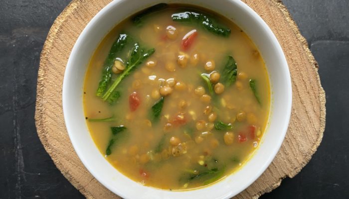 yellow-colored lentil dal soup in a white bowl against a black background.