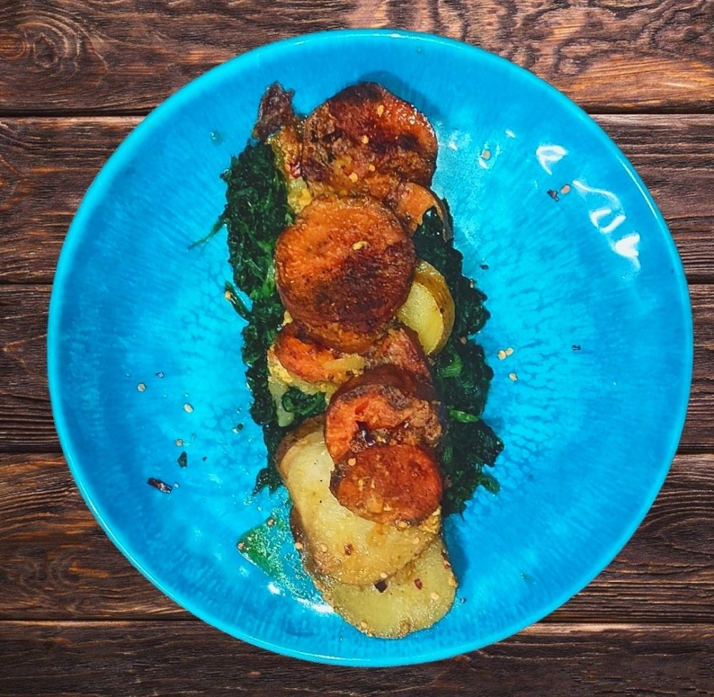 scalloped potatoes and spinach in a blue bowl with a brown wooden background