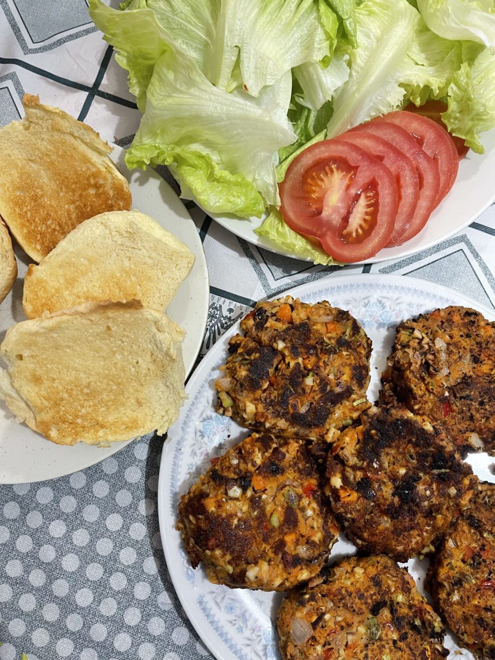 Plates of vegan burgers, bread, and toppings against a gray and white background