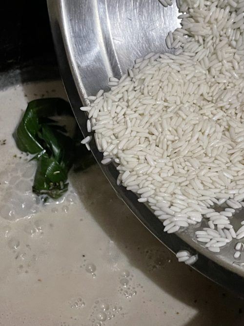 rice in a silver bowl next to a pot simmering with coconut milk.