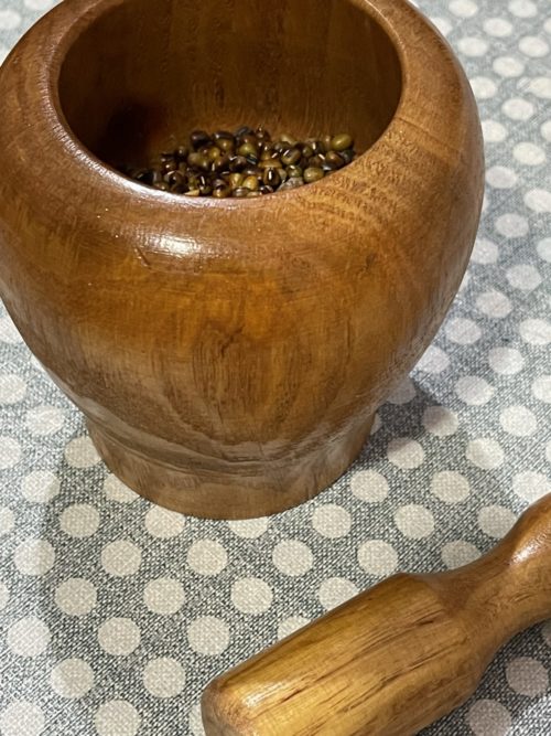 wooden mortar half filled with mung beans and a wooden pestle lying next to it.