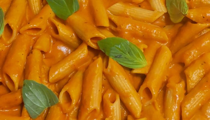 Vegan penne alla vodka in a creamy tomato sauce with basil leaves scattered on top.