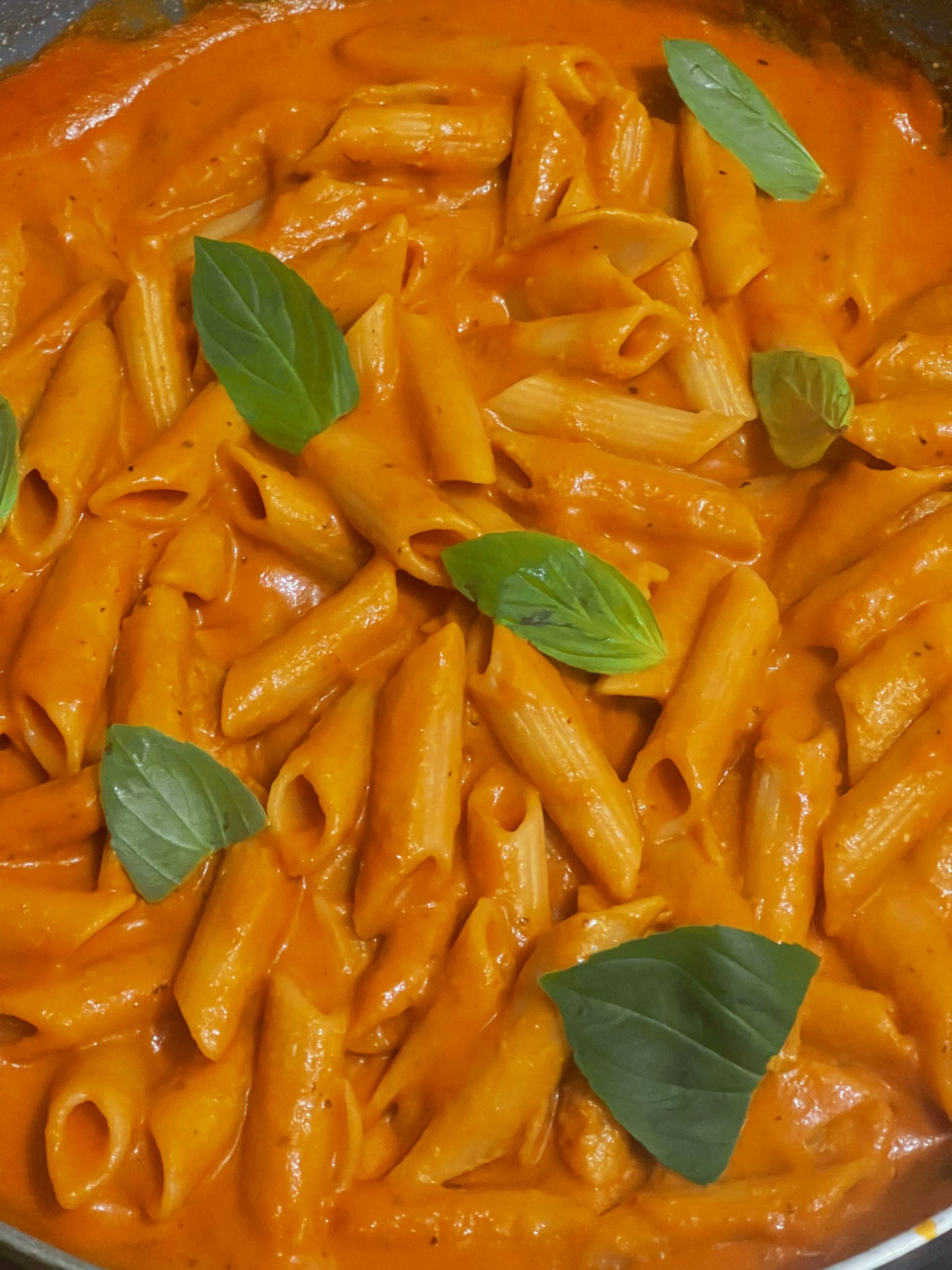 Vegan penne alla vodka in a creamy tomato sauce with basil leaves scattered on top.