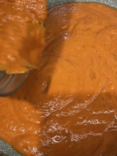 pouring tomato sauce with vodka and vegan cream into a pan