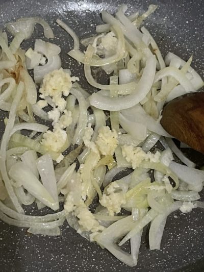 minced garlic and onion slices cooked half way through in a pan.