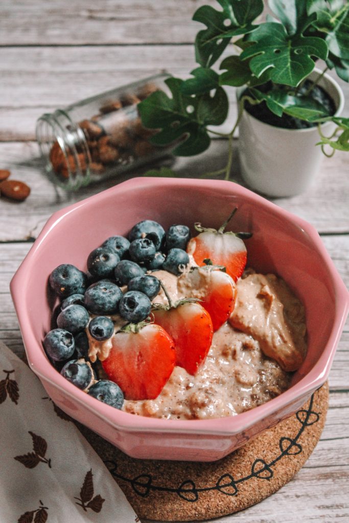 oatmeal with strawberries and blueberries in a pink bowl on a pale wooden table. 